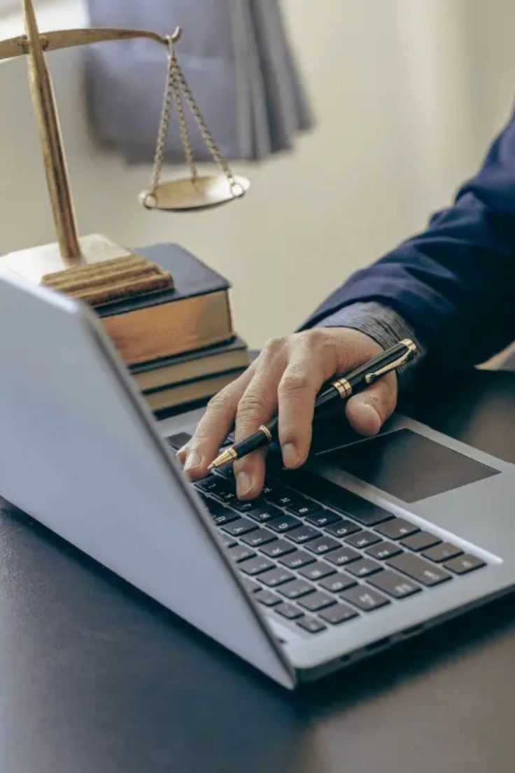 Advogado usando notebook para atendimento por videoconferência, ao lado de balança da justiça e livros